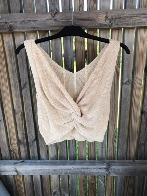 Beige stickad omlott linnetopp - Säljer en beige stickad linnetopp med omlottdetalj framtill. Toppen är ärmlös och har en djup v-ringning både fram och bak. Perfekt för varma dagar och enkel att styla med jeans eller kjol.