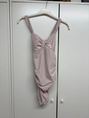 Ljusrosa baddräkt med knyt i ryggen - Säljer en ljusrosa baddräkt med breda axelband och snygg knytning i ryggen. Baddräkten har en feminin skärning och är tillverkad i ett stretchigt material som passar perfekt för strand eller pool. Enkel men stilren design som känns modern. 