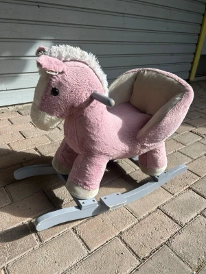 Gungande mjukishäst rosa - Söt gungande mjukishäst i rosa plysch med vita detaljer och mjuk sits. Hästen har handtag i plast och stabila gråa medar i trä. Perfekt för små barn som vill leka och gunga inomhus.