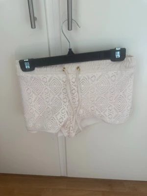 Crenefärgade spets-shorts med snörning - Säljer ett par shorts med snygg spetsdetalj och snörning i midjan. De har elastisk midja och är perfekta för varma dagar. Shortsen har en feminin look med sitt spetsmönster och är riktigt bekväma.