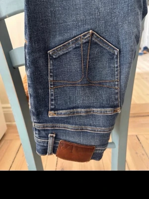 Tiger of Sweden jeans - Säljer ett par klassiska blå jeans. Jeansen har fem fickor och en brun läderpatch bak i midjan. Passar perfekt till en avslappnad stil och är tillverkade i slitstarkt bomullsmaterial.