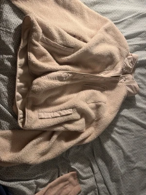 Beige teddyjacka med knappar - Supermjuk och fluffig teddyjacka i beige färg med dragkedja och tryckknappar framtill. Jackan har två fickor med lock och hög krage som håller dig varm. Perfekt för kyliga dagar och riktigt cozy vibe.