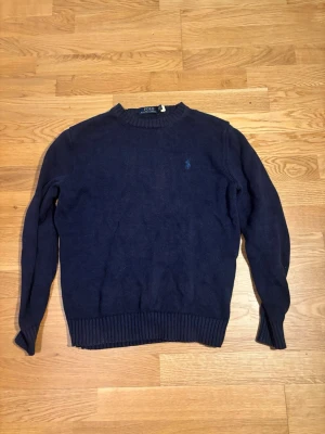 Navy Polo Ralph Lauren Stickad Tröja - Klassisk och tidlös stickad tröja från Polo Ralph Lauren i en snygg marinblå nyans. Ett basplagg i varje garderob som passar till allt. Storlek S men sitter som en XS nu 