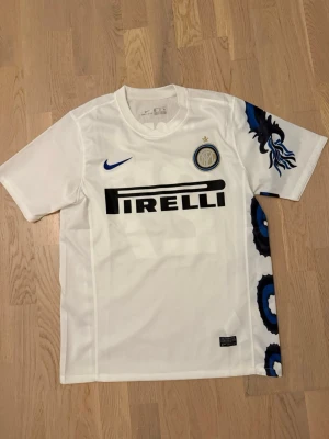Inter Milan bortatröja Nike - Säljer en vit Inter Milan bortatröja från Nike med blått och svart drakmönster på sidan. Tröjan har Pirelli-logga på bröstet, klubbmärke och blå Nike-swoosh. På ryggen står det PANDEV och nummer 27 i blått. Storlek M