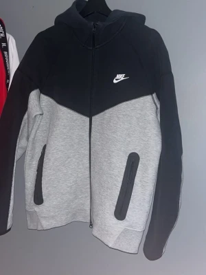 Nike tech fleece hoodie - Säljer en äkta Nike Tech Fleece zip hoodie i grå/svart.  * Storlek: M * Färg: Grå/Svart * Bra skick, inga hål eller större defekter. * Dragkedjor och fickor fungerar som de ska. * Perfekt till både vardag och träning. Priset är ej hugget i sten.