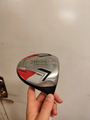 Spalding Executive golfklubba - Golfklubba Spalding Executive 460cc med huvudet i silverfärgad metall, detaljer i rött och svart. Klubban har en bred träffyta och modern design, perfekt för dig som vill ha extra kraft i slagen. Snygg och sportig look för golfbanan. Liten skavank på klubbhuvudet annars inget fel