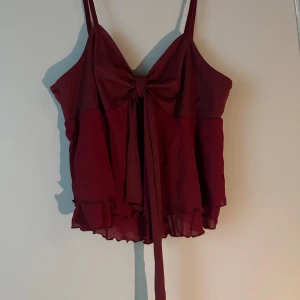 Vinröd linnetopp med rosett och volang - Supersöt vinröd linnetopp med smala axelband, stor rosett framtill och volangkant nertill. Toppen har en flowy passform 🌺🌸