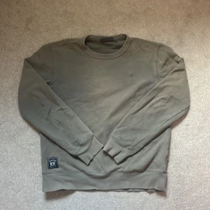 Olivgrön sweatshirt från Morris XS - Olivgrön sweatshirt från Morris Stockholm i storlek XS. Tröjan har rund hals, ribbade muddar och en broderad logga på bröstet. Nedtill finns en snygg patch med Morris Luxury Sports Goods. Perfekt för chill dagar och enkel att matcha. 1200 nypris