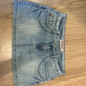 Ljusblå jeanskjol från LONNY - Säljer en kort ljusblå jeanskjol från LONNY med klassiska fickor fram och bak, snygga sömmar och coola detaljer på bakfickorna. Kjolen har knapp och dragkedja framtill samt bälteshällor. Väldigt älskad kjol men i helt ok skick. 