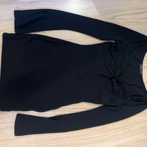 Svart långärmad kortklänning - Svart klänning från shein med lång ärm och tight passform. Modellen är kort och har en twistad detalj vid bysten som ger extra stilpoäng. Perfekt för dig som gillar minimalistisk look med en liten edge. Aldrig använt.
