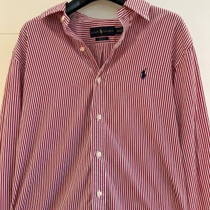 Rödvit randig skjorta från Ralph Lauren - Snygg skjorta från Ralph Lauren i custom fit med röda och vita vertikala ränder. Klassisk krage, långärmad och med knappar framtill. Broderad marinblå logga på bröstet. Hör gärna av dig vid funderingar! :)