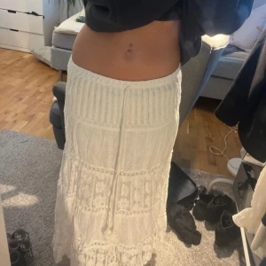 Vit långkjol med spets och snörning - Säljer en superfin vit långkjol med spetsdetaljer och snörning i midjan. Kjolen har flera lager med broderade mönster och volanger som ger en bohemisk vibe. Perfekt för dig som gillar romantisk och feminin stil.
