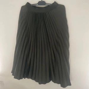Svart plisserad kjol från H&M - Snygg olivgrön plisserad kjol från H&M i storlek 34. Kjolen har ett elastiskt midjeband och ett klassiskt veckat tyg som ger en stilren och trendig look. Perfekt att matcha med en croppad topp eller stickad tröja.