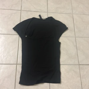 Svart topp från H&M Divided XXS - En svart enkel topp från H&M Divided i storlek XXS. Modellen har korta ärmar och rund halsringning. Tunt och mjukt material som känns skönt mot huden, perfekt för en clean och stilren look.