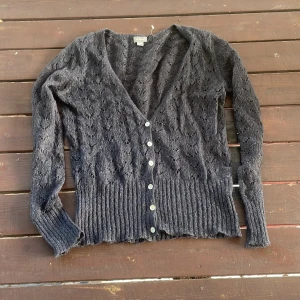 Mörkblå glittrig stickad kofta från Lindex - Mysig mörkblå glittrig stickad kofta från Lindex med v-ringning och fina pärlemorknappar. Koftan har ett hålmönster och bred ribbad kant nedtill och vid ärmsluten. Perfekt att slänga över en topp för en chill look.