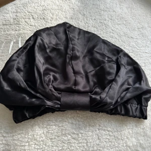 Svart satinmössa från Urban Hair - Aldrig använt säljer pågrund av råkat köpa två likadana modeller. Snygg svart satinmössa från Urban Hair Accessories. Mössan har en glansig finish och elastisk kant som håller den på plats. Perfekt för att skydda håret under natten eller när du vill ha en chill look. Klassisk design med diskret logga invändigt.