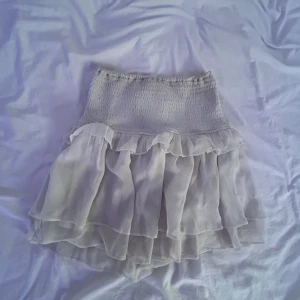 Ljusvit volangkjol med resår - Supersöt kort kjol i ljusvit färg med flera lager volanger och bred smockresår i midjan.