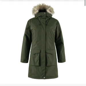 Grön parkasjacka med fuskpäls från Fjällräven - helt ny och oanvänd! 💕Snygg mörkgrön parkasjacka från Fjällräven med huva och fuskpäls i storlek M. Jackan har stora fickor framtill, dragkedja och knappar, samt justerbar huva. Perfekt för kalla dagar med sin långa modell och varma känsla. Nypris är 5999kr💞