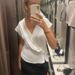 Vit omlottopp med knyt - Säljer en stilren vit omlottopp med knyt i sidan och v-ringning. Toppen har korta ärmar och en lätt, flowy passform som ger en fräsch och clean look. Perfekt att styla med kjol eller jeans för en trendig vibe.