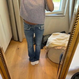 Blå bootcut jeans med fransade detaljer - Säljer ett par blå bootcut jeans med låg midja och fransade kanter vid fickorna. Jeansen har klassisk femficksdesign och är tillverkade i denim. Snygg slitning och coola detaljer som ger en avslappnad vibe. Dem är lite uppsydda,jag är 163