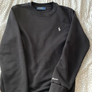 Svart sweatshirt från Polo Ralph Lauren - Svart sweatshirt från Polo Ralph Lauren med klassisk rund hals och broderad logga på bröstet. Ärmen har snyggt broderat Ralph Lauren-tryck. Tröjan är i mjuk bomull och har långa ärmar med ribbade muddar. Perfekt för en clean och stilren look. Pris kan diskuteras!!