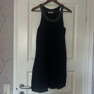 Svart klänning från Mango - Svart klänning från Mango med snygg pärl- och paljettdekor runt halsringningen. Klänningen har en rak passform och avslutas med små bollar längs fållen för en extra detalj. 