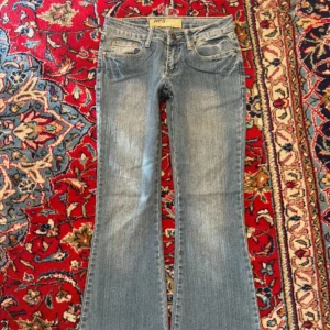 Blå low waist bootcut jeans - Snygga blå bootcut jeans från HIPS med slitningar och coola nitar på bakfickorna. Midja:34 Stuss:38 Gren:19 Lårbredd:21 Innerbenslängd:76 Benvidd:27  