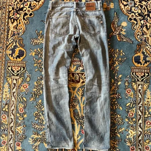 Blå jeans från Edwin med raka ben - Säljer ett par klassiska blå jeans från Edwin med raka ben och snygga slitningar. Jeansen har fem fickor, gylf med knapp och dragkedja samt kontrastsömmar. Perfekta för dig som gillar en tidlös och avslappnad stil.