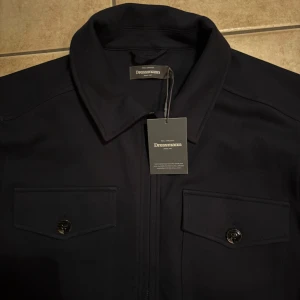 Overshirt - Säljer nu min sprillans nya snygga mörkblå overshirt från Dressmann med klassisk krage och två stora bröstfickor med knappar. Jackan har dragkedja framtill och är långärmad. Perfekt för dig som gillar stilrena och enkla plagg som funkar till alla tillfällen! Jackan är helt ny med prislappen på, aldrig använd!! Prutat och klart😇