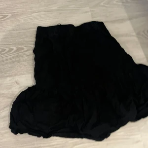 Svart volangkjol med resårmidja - Säljer en svart kortkjol med volangkant och bred resår i midjan. Kjolen har en loose passform och är perfekt för dig som gillar en enkel men ändå cool stil. Materialet känns lätt och flowy, vilket gör den skön att bära under varmare dagar.