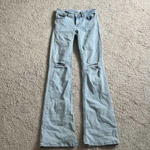 Bootcut jeans i ljus denim från Nelly - Bootcut jeans i ljusblå denim från Nelly med slitna knän och snygga rosa broderade detaljer på bakfickorna. Klassisk femficksmodell med låg midja och vida ben. Perfekta för dig som gillar en retro vibe och vill sticka ut lite extra.