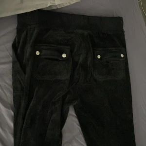 Svarta mjukisbyxor med snörning - Svarta mjukisbyxor i mjukt material med bred resår i midjan och snörning framtill. Byxorna har två bakfickor med lock och silverfärgade knappar. Perfekta för chill dagar eller när du vill vara extra bekväm.