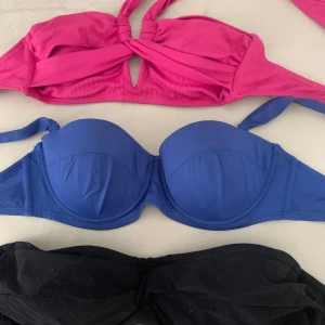 Tre bikiniöverdelar i olika färger - Säljer tre snygga bikiniöverdelar: en ribbad rosa bandeau med twist och knyt, en blå vadderad bikini-bh med bygel och knyt i nacken samt en svart bandeau med twist framtill. 1st för 30kr   2st för 45kr  3st för 55kr