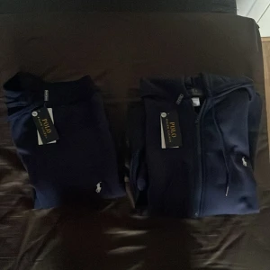 Mörkblå mjukisbyxor och mörkblå zip hoodie från Polo Ralph Lauren - En helt ny mörkblå zip hoodie från Polo Ralph Lauren som aldrig har använts som kommer med helt nya mörkblå mjukisbyxor som inte heller har använts. Båda med prislapp och i storlek S