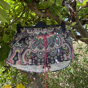 Mönstrade shorts från Odd Molly - Snygga shorts från Odd Molly med färgstarkt paisleymönster i blått, rosa, grönt och vitt. Modellen har midwaist, elastisk midja med rosa snörning och en liten ficka bak. Perfekta för varma sommardagar och riktigt chill stil. Storlek 3 som enligt deras storleksguide motsvarar en storlek L. Kan vara något små i storlek.  Mycket fint skick, jag hittar inga synliga anmärkningar eller defekter. 