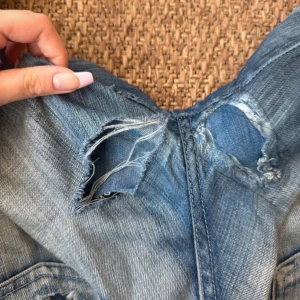 Victoria Beckham bootcut jeans med broderi - Säljer ett par blå bootcut jeans från Victoria Beckham för Rock & Republic. Jeansen har hål vid rumpan som man kan se på sista bilden. 