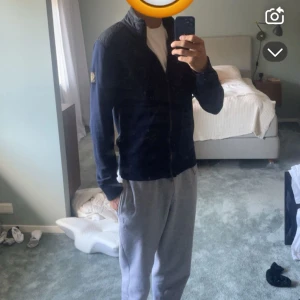 Mörkblå stickad kofta från Belstaff - Snygg mörkblå stickad kofta från Belstaff med dragkedja framtill och quiltade detaljer på axlarna. Storlek S/M. Långärmad modell med ribbade muddar och diskret logga på ärmen. Perfekt för lager-på-lager men funkar även som en vanlig chill övertröja