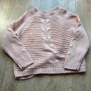 Ljusrosa stickad tröja med flätmönster - Superfin ljusrosa stickad tröja med breda flätor framtill och på ärmarna. Tröjan har rund halsringning, ribbade muddar och en lite loose passform. Perfekt för dig som gillar mysiga och trendiga plagg med snygga detaljer.