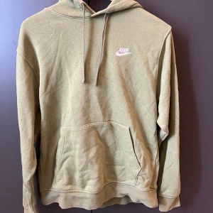 Mörkgröb hoodie från Nike med logga - Snygg grön hoodie från Nike med broderad vit logga på bröstet. Klassisk känguruficka framtill, dragsko i huvan och mjukt bomullsmaterial. Perfekt för en chill och avslappnad stil.