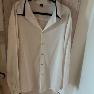 Vit skjorta med svarta detaljer Manfinity XL - Vit skjorta från Manfinity i storlek XL med svarta kontrastdetaljer på krage och manschetter. Klassisk passform, långa ärmar och knäppning framtill. Perfekt för dig som vill ha en stilren look med en twist.