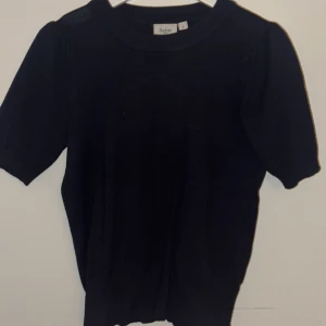 Svart stickad topp från Saint Tropez - En svart stickad topp från Saint Tropez med rund halsringning och korta ärmar. Modellen har en klassisk passform och ribbade muddar vid hals och ärmslut. Perfekt att styla med jeans eller kjol för en clean look.