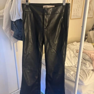 Svarta bootcut byxor i skinnimitation XS - Säljer ett par svarta bootcut byxor från Bershka i skinnimitation. Byxorna har en snygg, slät yta och en bakficka med minimalistisk design. Perfekta för dig som vill ha en edgy vibe och gillar trendiga material.