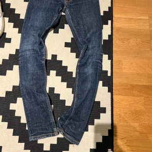 Mörkblå skinny jeans från Nudie - Snygga mörkblå skinny jeans från Nudie med klassisk orange söm på bakfickorna och läderpatch i midjan. Jeansen har smal passform, raka ben och är tillverkade i slitstarkt denim. Perfekt för dig som gillar en clean och stilren look.