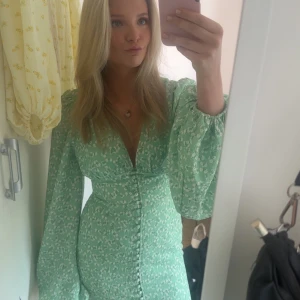 Grön adoore klänning  - Säljer en superfin grön adoore positano långklänning som inte säljs längre  med vita små blommor, v-ringad och med puffiga långärmar. Perfekt för vår och sommar o bröllop 