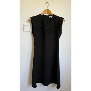Svart klänning Les Petites Paris - Snygg svart klänning från Les Petites Paris i storlek 36. Modellen är ärmlös med rund hals och har diskreta dekorativa sömmar framtill. Klänningen har en smickrande A-linjeform och stängs med dragkedja i ryggen. Perfekt för dig som gillar stilrena och klassiska plagg.