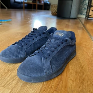 Mörkblå mocka sneakers från Polo - Snygga mörkblå sneakers från Polo Ralph Lauren i mjuk mocka med rund tå och platt sula. Skorna har klassisk snörning och Polo-logga på plösen. Perfekt för dig som gillar stilrena och bekväma sneakers med en exklusiv känsla.