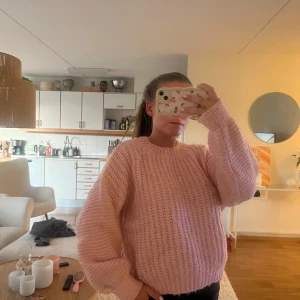 Ljusrosa stickad tröja med loose fit - Supermysig ljusrosa stickad tröja med loose passform och rund hals. Tröjan har långa ärmar och ett fluffigt, ribbat mönster som gör den extra cozy. Perfekt för dig som gillar oversized.