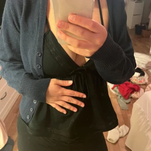 Mörkblå stickad kofta med knappar - Mysig mörkblå stickad kofta med djup v-ringning och knappar hela vägen framtill. Koftan har långa ärmar och ribbade muddar vid ärmslut och nederkant. Perfekt att slänga över en topp för en chill look.