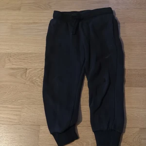 Svarta mjukisbyxor från H&M - Svarta mjukisbyxor från H&M med resår och snörning i midjan. Byxorna har ribbade muddar vid bensluten och är gjorda i mjukt material som är skönt att ha på sig. Perfekta för chill dagar eller när du vill vara bekväm.(litet hål i knät) 