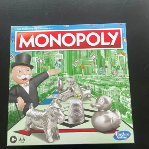 Monopol brädspel från Hasbro Gaming - Klassiska Monopol från Hasbro Gaming. Innehåller spelplan, spelpjäser i metall, tärningar, spelkort, papperspengar samt gröna hus och röda hotell. Perfekt för 2-6 spelare från 8 år och uppåt.